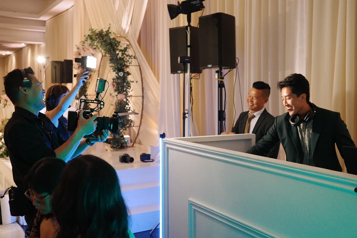 Professional DJ setup at elegant wedding reception with white draping, illuminated speakers, and white DJ booth