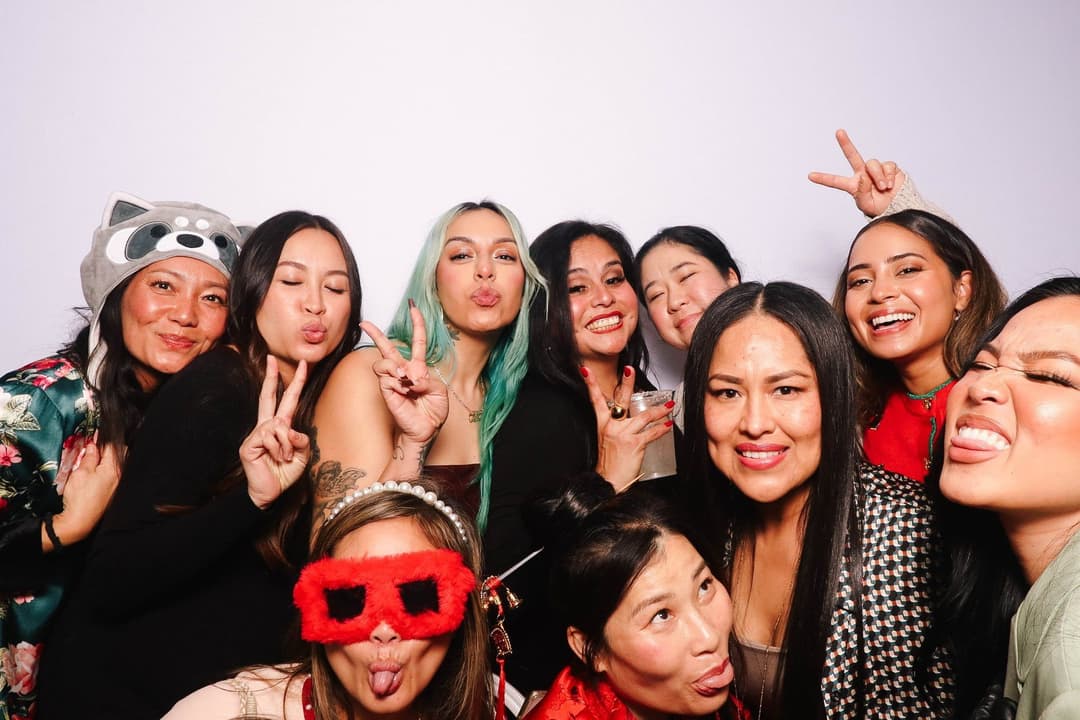 Group of young women having fun with colorful photo booth props including animal mask, peace signs, and silly expressions