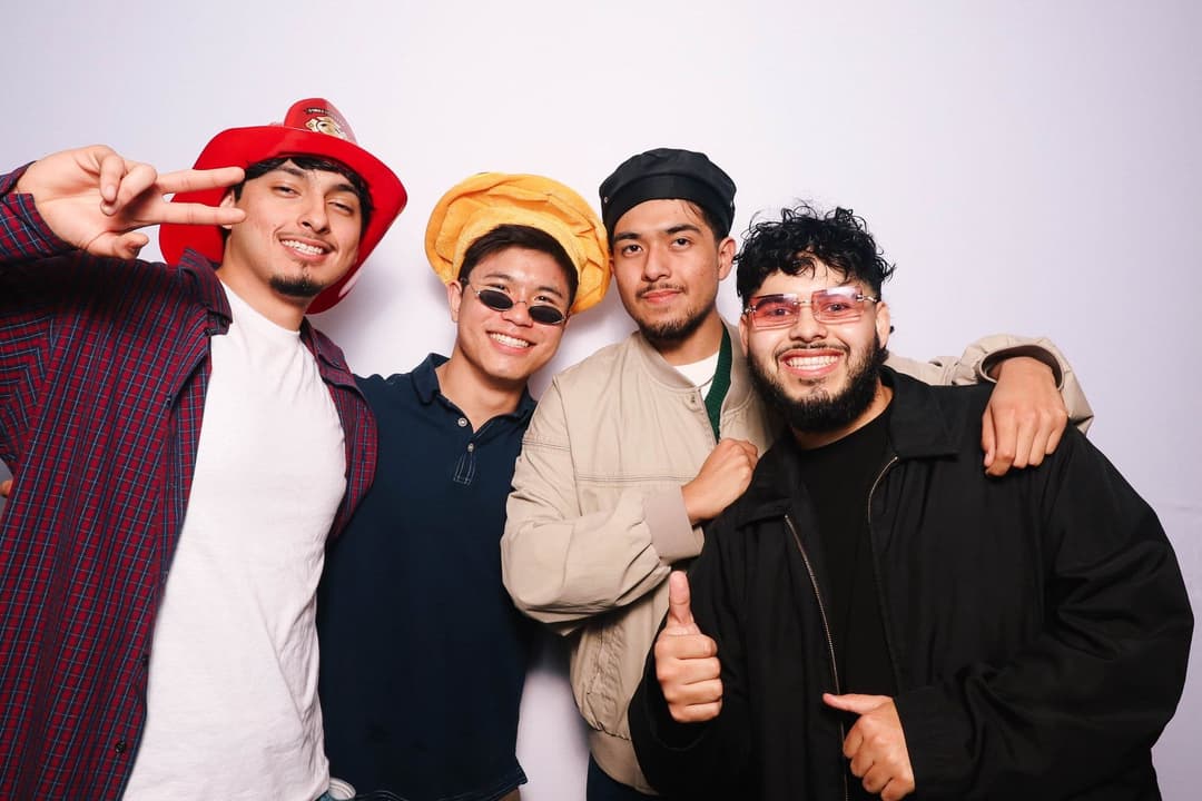 Five young men posing together wearing colorful hats and sunglasses with thumbs up and silly expressions