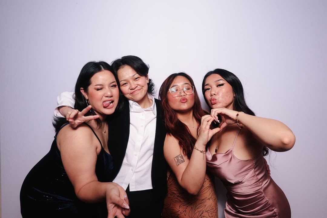 Four young women making kissy faces and peace signs in elegant outfits against white backdrop