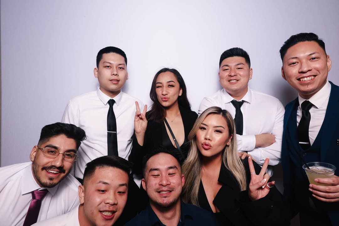 Large group of formally dressed wedding guests posing together with peace signs and drinks