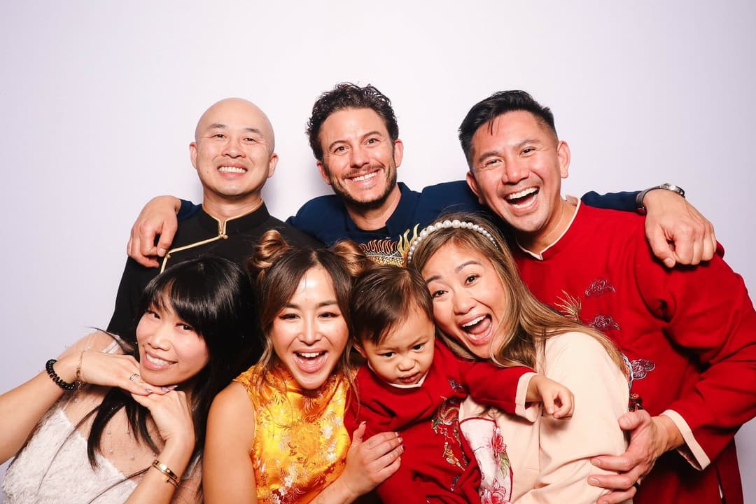 Large group of friends celebrating in red and gold traditional outfits with laughing expressions and playful poses