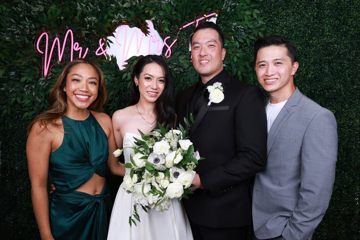 Bride and groom with wedding party posing against green backdrop with 'Mr & Mrs' neon sign