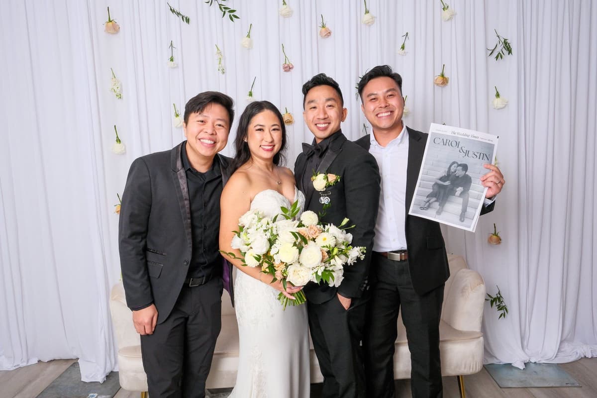 Bride and groom with wedding party posing against white backdrop with hanging floral elements