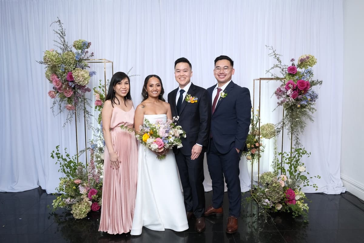 Bride in white gown and groom with wedding party posing with ornate gold frames and purple floral arrangements